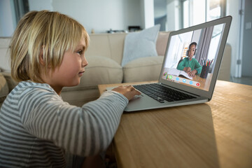 Caucasian boy using laptop for video call, with elementary school pupil on screen