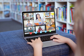 Caucasian girl using laptop for video call, with smiling diverse high school pupils on screen