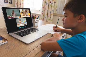 Fototapeta na wymiar Caucasian boy using laptop for video call, with smiling diverse elementary school pupils on screen