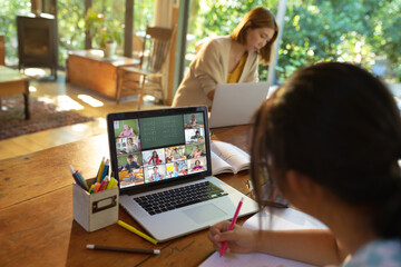 Asian girl using laptop for video call, with smiling diverse elementary school pupils on screen