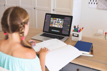 Caucasian girl using laptop for video call, with diverse elementary school pupils on screen