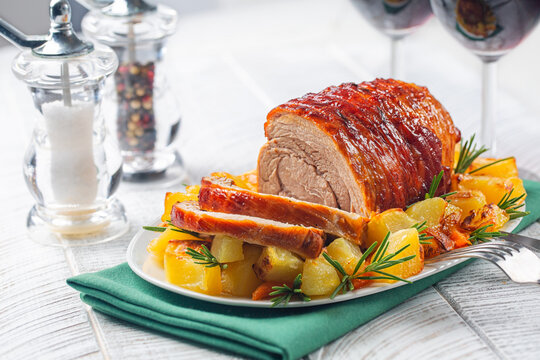 Baked veal roulade with potato and rosemary. Red wine glasses on a white wooden table.