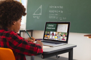 African american boy using laptop for video call, with diverse elementary school pupils on screen