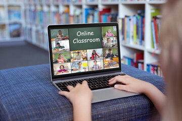 Caucasian girl using laptop for video call, with smiling diverse elementary school pupils on screen