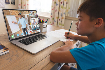 Caucasian boy using laptop for video call, with smiling diverse high school pupils on screen