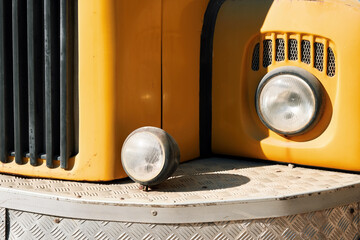 Front view detail of a vintage yellow truck with round headlights.