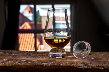 Dram of single malt scotch whisky served in tasting glass with view on old window and houses