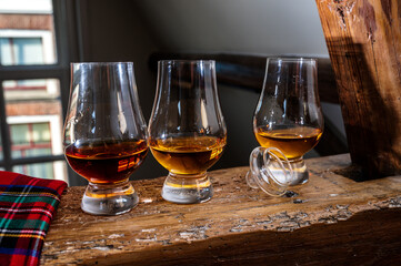 Dram of single malt scotch whisky served in tasting glass with view on old window and houses and red tartan