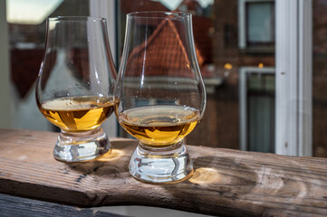 Dram of single malt scotch whisky served in tasting glass with view on old window and houses