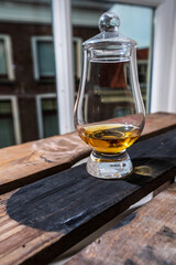 Dram of single malt scotch whisky served in tasting glass with view on old window and houses