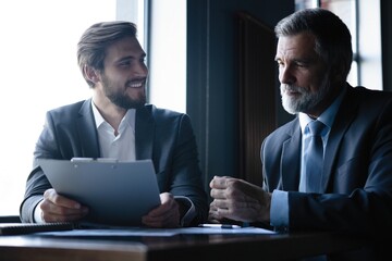 Senior and junior businessman discuss something during their meeting, office background.