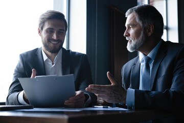 Senior and junior businessman discuss something during their meeting, office background.