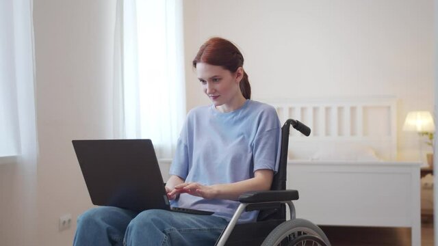 A disabled woman is sitting in her wheelchair and looking through the Internet 