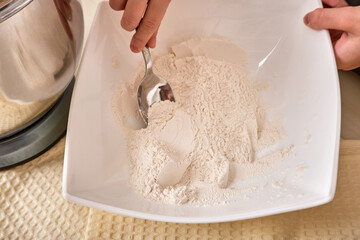 A teenage girl cooks a homemade cake in the kitchen. Mixes the ingredients for the cake in an electric mixer. The hand lays the ingredients in the mixer. Close-up. High quality photo
