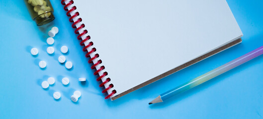 White medical pills and tablets spilling out of a drug bottle on a blue background. Medical layout pill, notebook and pencil. banner