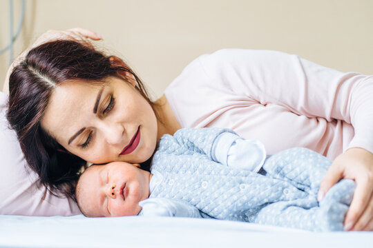 Middle age mother relaxing with her newborn baby boy on bed at home. Beautiful conceptual image of Maternity. First moment of life.