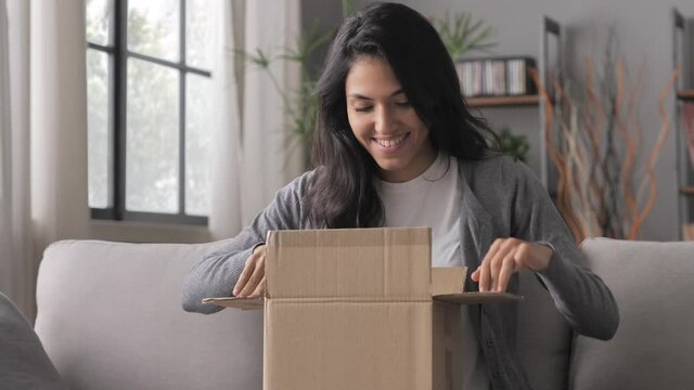 excited young woman on the sofa at home opening postal parcel box,millennial girl unpack package purchased online,e-commerce internet shopping concept