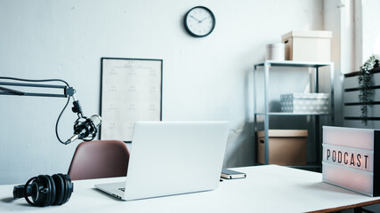 Local podcast studio interior. Microphone, laptop, white desk and cozy streaming workplace
