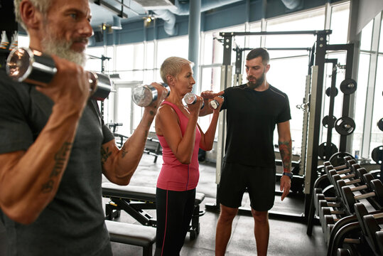 Determined senior woman and man with dumbbells in gym