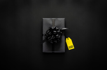A black gift box with ribbon and yellow price tag puts on black background. Black friday concept.