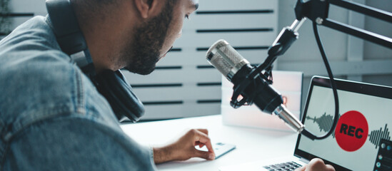 Handsome mixed race host streaming his audio podcast using microphone and laptop at his homemade...
