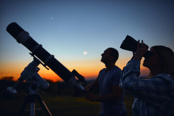 Couple stargazing together with a astronomical telescope. - obrazy, fototapety, plakaty
