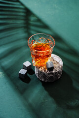 Hard strong alcoholic drinks in glass: cognac, tequila, scotch, brandy or whiskey on a green background with hard lights and shadows, top view