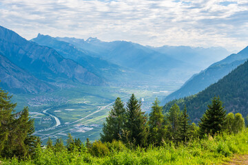 Vue de la vallée du Rhône depuis Saxon sur les hauteurs de la luy en Suisse avec des sapins, et un massif forestier par un jour ensoleillé avec des nuages © Guillaume