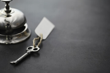 A shiny silver metal bell at the hotel reception. A table in the hotel at the concierge with a bell and a door key. Key and bell in a hotel.