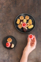 Female hand hold Panellet  and different Panellets on the black plate on concrete background. Catalonian dessert for Castanyada (All Saints Day).