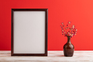 Wooden frame with purple barrenwort flowers in ceramic vase on red pastel background. side view, copy space, mockup.