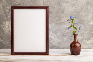 Wooden frame with blue forget-me-not flowers in ceramic vase on gray concrete background. side view, copy space, mockup.