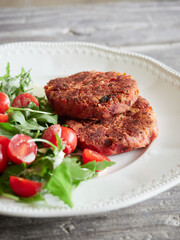 close up view of veggie burgers and rocket cherry tomatoes salad served on a white plate on a wooden table. Meat alternative.