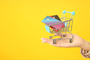 Female hand holds shop trolley with credit cards on yellow background