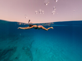 Half underwater shot of woman snorkeling in crystal water