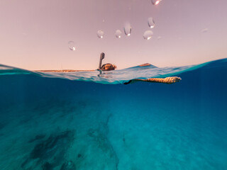 Half underwater shot of woman snorkeling in crystal water