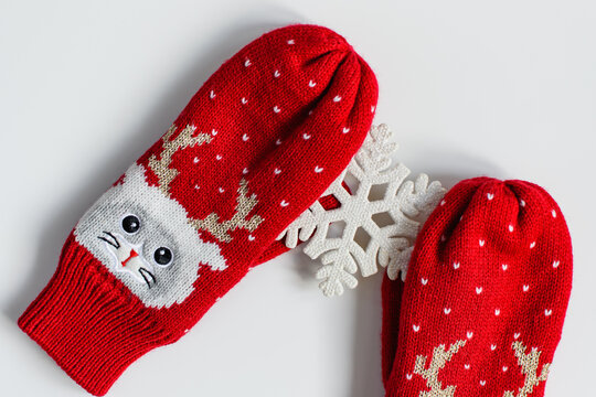A pair of red woolen knitted soft mittens with cat faces and deer antlers hold a snowflakeon a white background . The concept of New Year's holiday and Christmas. Flat lay, top view.