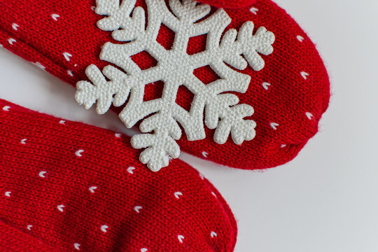 A pair of woolen woolen mittens for winter and a symbol of winter white snowflake on a white background. New year and christmas holiday flat lay. Protection from cold and snow.