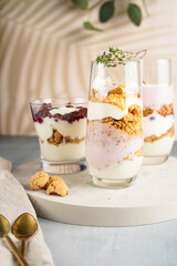 Three glasses with a layered creamy yoghurt dessert trifle with cookies, amaretti, cherries and thyme in a tropical setting