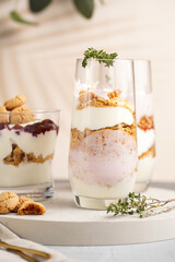 Three glasses with a layered creamy yoghurt dessert trifle with cookies, amaretti, cherries and thyme in a tropical setting
