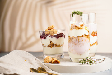 Three glasses with a layered creamy yoghurt dessert trifle with cookies, amaretti, cherries and thyme in a tropical setting