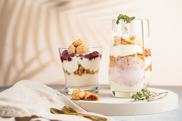 Three glasses with a layered creamy yoghurt dessert trifle with cookies, amaretti, cherries and thyme in a tropical setting