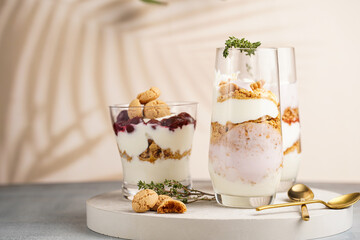 Three glasses with a layered creamy yoghurt dessert trifle with cookies, amaretti, cherries and thyme in a tropical setting