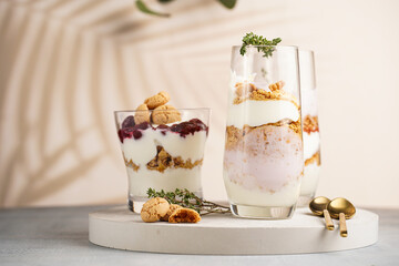 Three glasses with a layered creamy yoghurt dessert trifle with cookies, amaretti, cherries and thyme in a tropical setting