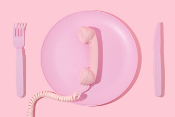 Creative layout with pastel pink plate, fork,knife,retro telephone handset on pastel pink background. Minimal surreal breakfast idea or food restaurant concept.  80s or 90s aesthetic fashion idea.