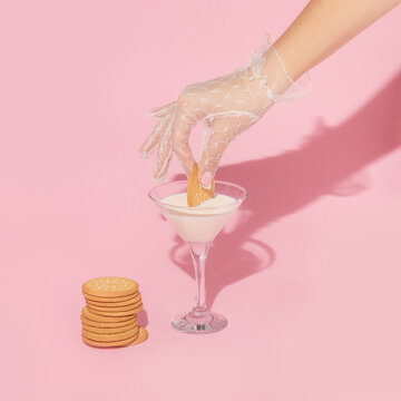 Creative layout with hand in white lace glove  dipping cookie in milk in martini cocktail glass. 80s or 90s retro aesthetic fashion concept. Romantic valentines day drink idea.