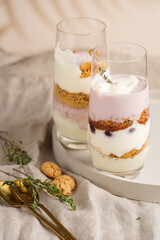 Obraz na płótnie Canvas Two tall glasses with a layered creamy yoghurt dessert trifle with cookies, amaretti, cherries and thyme on a concrete tray