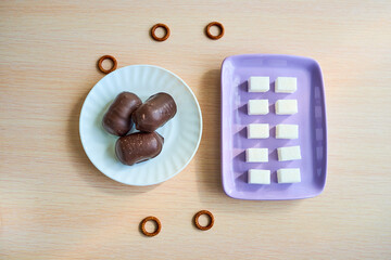 A purple plate with ten pieces of white sugar and a white plate with three chocolates are on the table. Top view