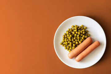 Sausages with green peas on a colored background. Top view.