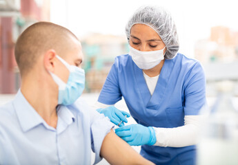 Doctor woman giving coronavirus vaccine to european middle-aged man in vaccination center